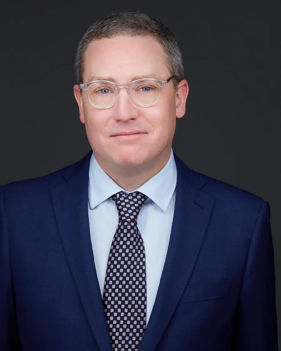 Chivers Carpenter staff headshot, Edmonton: glasses, a navy suit and patterned tie, on charcoal