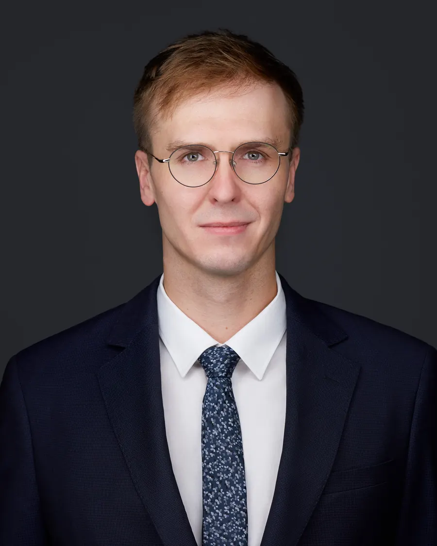 Chivers Carpenter staff headshot, Edmonton: glasses, a dark suit and blue tie, on charcoal